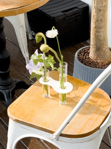 Close-up of minimalist test tube flower vase on wooden chair in a sunlit outdoor patio