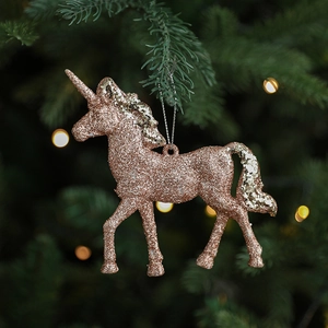 Pink glitter unicorn Christmas ornament hanging on a pine tree branch with bokeh lights