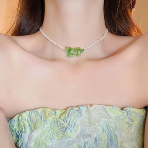 Detail of pearl necklace featuring a green crystal butterfly pendant on a female model
