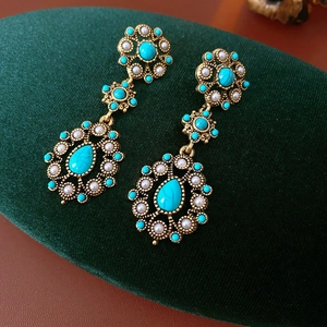 Detail of vintage gold earrings with turquoise stones and pearls on green velvet