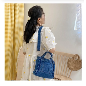 Lifestyle shot of blue denim shoulder bag with adjustable strap worn by a model indoors
