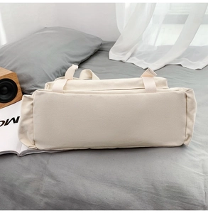 Vue détaillée du fond du sac en toile beige avec anses tissées sur un lit gris
