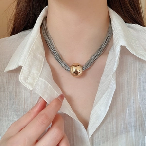 Close-up of layered silver chain necklace with a large gold ball pendant on a model