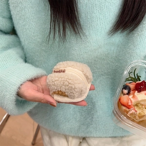 Close-up of beige plush lamb wool storage pouch with zipper held by hand outdoors