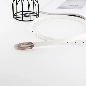White patent leather skinny belt with golden rhinestone buckle against minimalist props