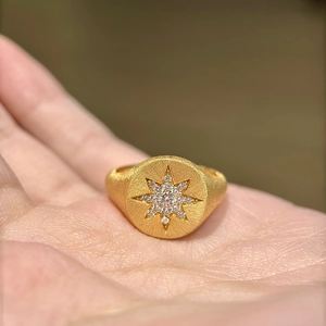 Detail of matte gold signet ring with starburst pattern and zircons held in hand