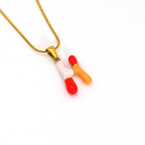 Macro detail of enamel H pendant in pink and orange tones with gold snake chain