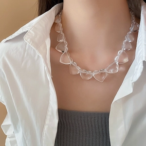 Detail of a transparent irregular heart acrylic necklace worn by a model in a white shirt