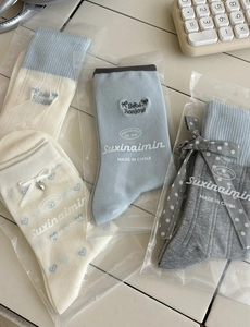 Flat lay of cream and blue cotton mid-calf socks with heart embroidery and bow details