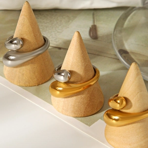 Dettaglio macro di anelli a goccia oro e argento con design fluido su supporti in legno