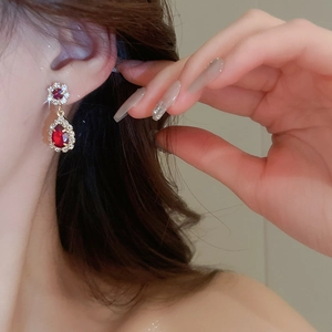 Close-up of elegant gold earrings with teardrop red gemstones and diamond accents