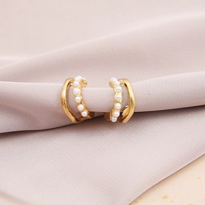 Elegant gold-plated C-shaped twisted metal earrings with white pearls on purple satin background