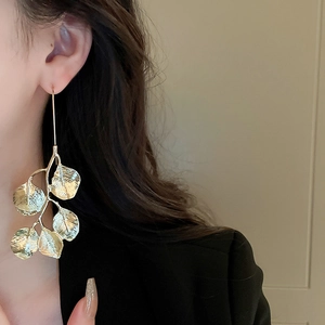 Close-up of a model wearing elegant long golden leaf earrings with a metallic finish