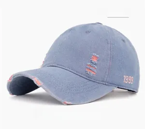 Detail of light blue washed denim baseball cap with pink 1999 embroidery and distressed holes