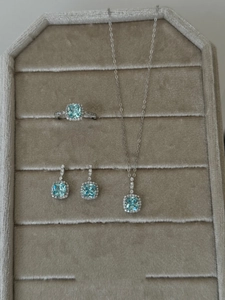 Detail view of silver jewelry set with square blue gemstones on a beige velvet tray