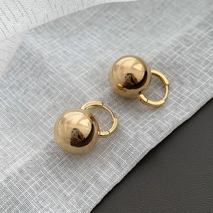 Macro shot of gold spherical leverback earrings on white linen and dark leather texture