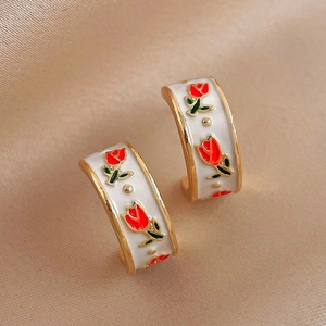 Detail of vintage gold C-shape earrings with white enamel and red rose floral patterns