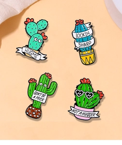 Detail of four enamel cactus pins with funny phrases on soft peach background