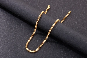 Macro shot of gold stainless steel box chain necklace with cylindrical clasp on black texture