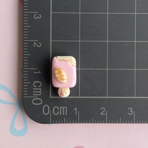 Close-up of a pink resin ice cream charm with a cat paw stick on a grid cutting mat