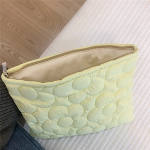 Detailed top view of light yellow quilted down makeup bag with floral embroidery texture