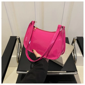 Detail of fuchsia patent leather underarm bag with gold zipper held by model