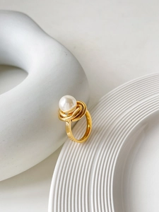 Détail d'une bague en titane doré avec une perle blanche et un anneau en métal tressé