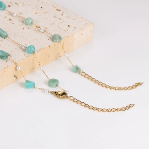 Gold necklace with irregular light green stones and pearls on beige stone plate