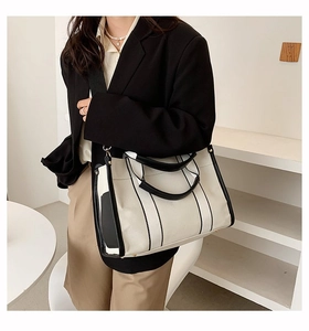 Detail of minimalist canvas tote bag with black trim showing cross-body strap and texture