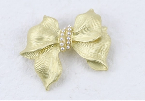 Macro shot of gold bow brooch with brushed matte finish and white faux pearl center inlay