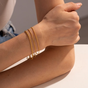 Detailed close-up of three layered gold chain bracelets including rope and snake link styles