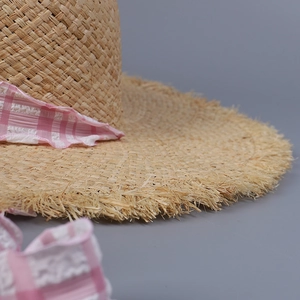 Close-up of woven raffia straw hat with pink checkered ribbon and frayed brim edges