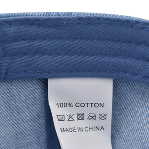 Detail view of the 100% cotton material tag and washing label on the blue baseball cap