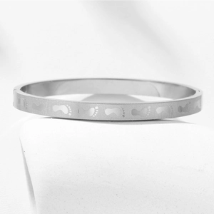 Macro detail of silver stainless steel bangle featuring engraved baby footprints pattern