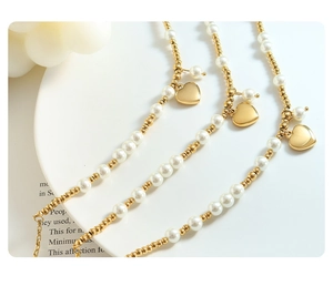 Macro view of handmade pearl necklace with gold heart pendant and beads on white tray