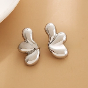 Macro detail of silver fluid teardrop earrings with a polished mirror finish on beige surface