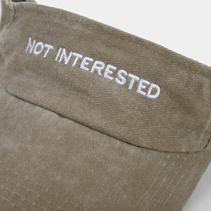 Detailed macro view of white embroidered 'NOT INTERESTED' slogan on washed canvas sun visor