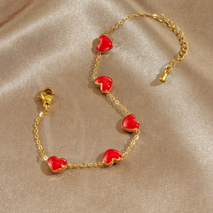 Gold chain bracelet with five red heart pendants displayed on a golden silk fabric background