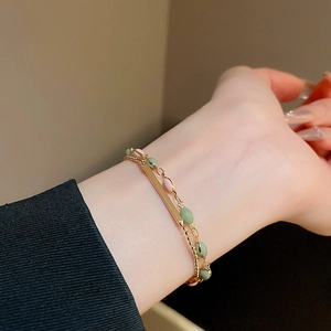 Detail of a double-layer gold-plated bracelet with green enamel beads on a woman's wrist