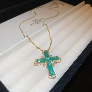 Détail d'un pendentif croix verte avec chaîne dorée et cristaux micro-pave