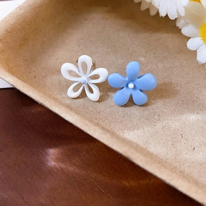 Détail de boucles d'oreilles asymétriques fleurs blanc et bleu clair sur plateau