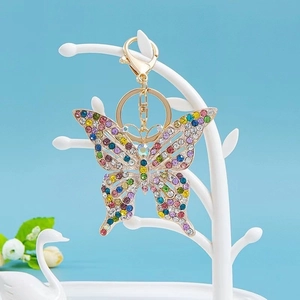 Dettaglio macro del portachiavi a fiocco dorato con cristalli colorati su supporto bianco