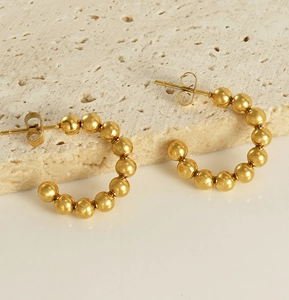 Detail of 18K gold-plated stainless steel beaded C-shaped hoop earrings on stone background