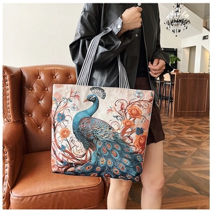 Detailed embroidery of peacock and flowers on canvas tote with striped handle strap