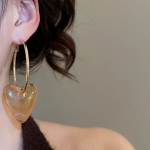Close-up of amber acrylic heart pendant on a gold hoop earring worn by a model