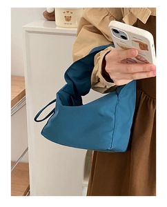 Détail du sac à nœud en tissu bleu canard tenu par un mannequin dans un cadre minimaliste