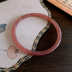 Vue détaillée d'un bracelet jonc en agate rose translucide sur un tissu brodé élégant