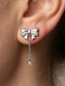 Close-up of elegant silver bow drop earring with fine chain on woman's earlobe
