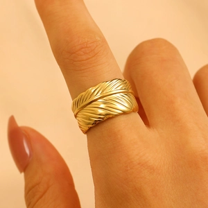 Close-up of a golden feather-shaped open ring featuring intricate metallic textures