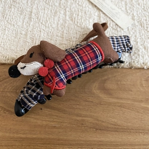 Detail of plush dachshund hair claw with red bow and plaid sweater on wood surface